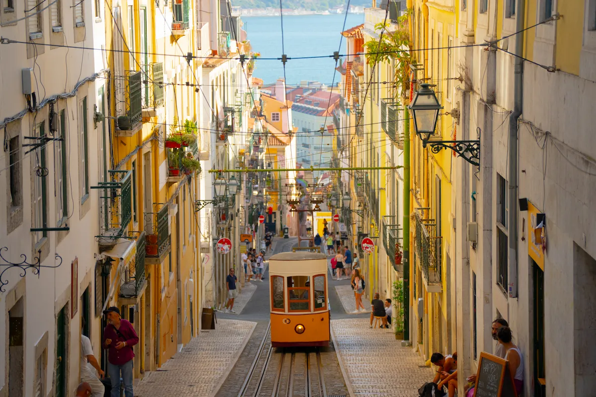 Tram 28 descending a narrow street between buildings at sunset in Lisbon, Portugal